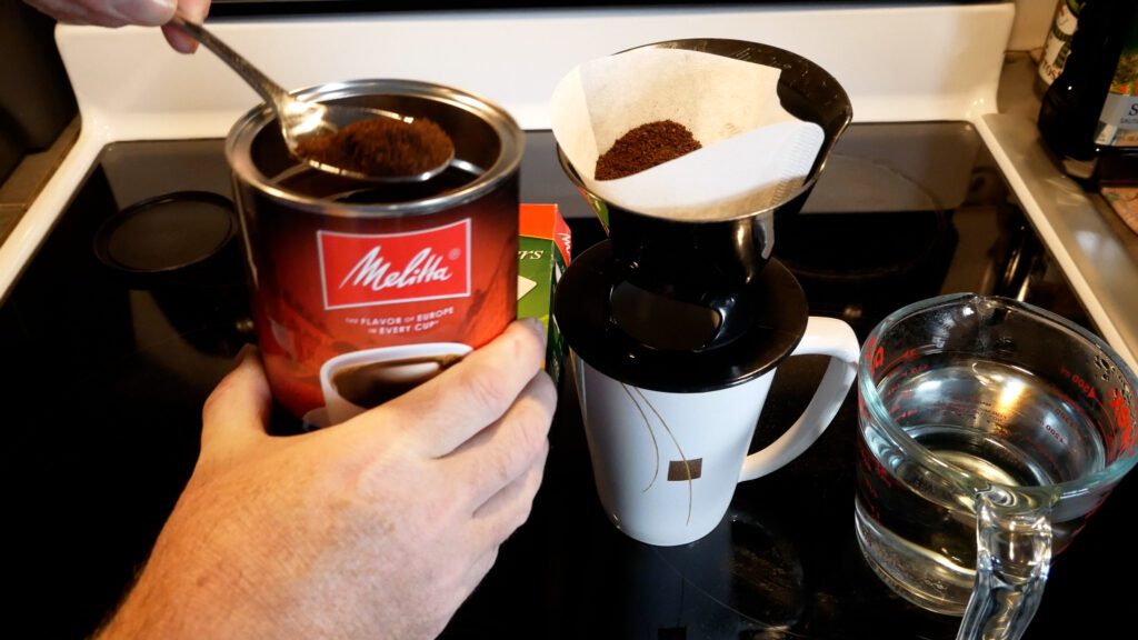 U Do It scooping Melitta Classic Blend ground coffee into the Melitta Super Premium #2 coffee filter that is in the Melitta Single Pour coffee brewer